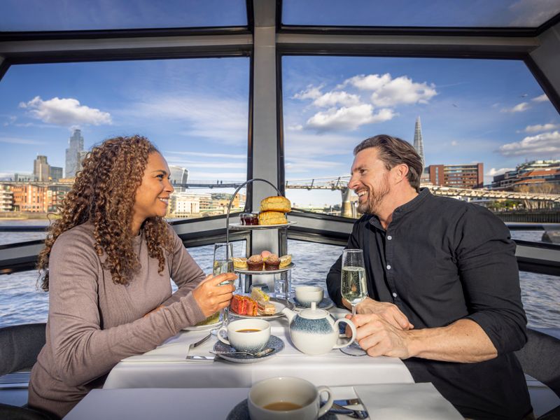 Paar genießt Afternoon Tea und Sekt während einer Themsefahrt mit Blick auf die Londoner Skyline und The Shard