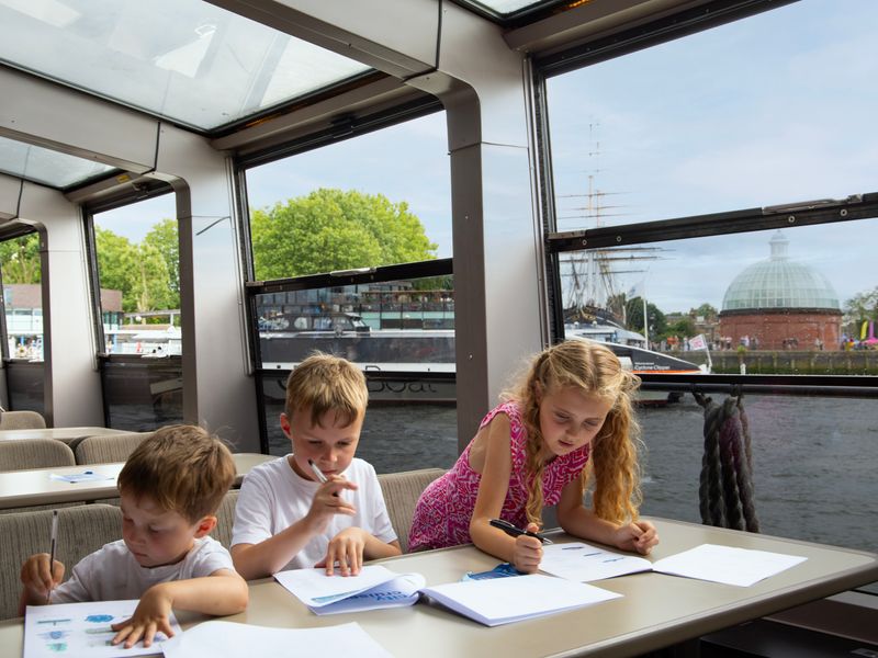 Drei Kinder schreiben etwas auf Papier auf Schiff in London