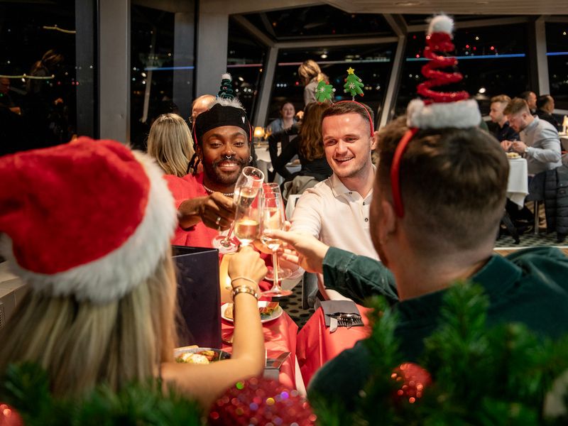 Gäste mit Weihnachtsmützen stoßen bei einer festlichen Dinner Cruise auf der Themse in London an
