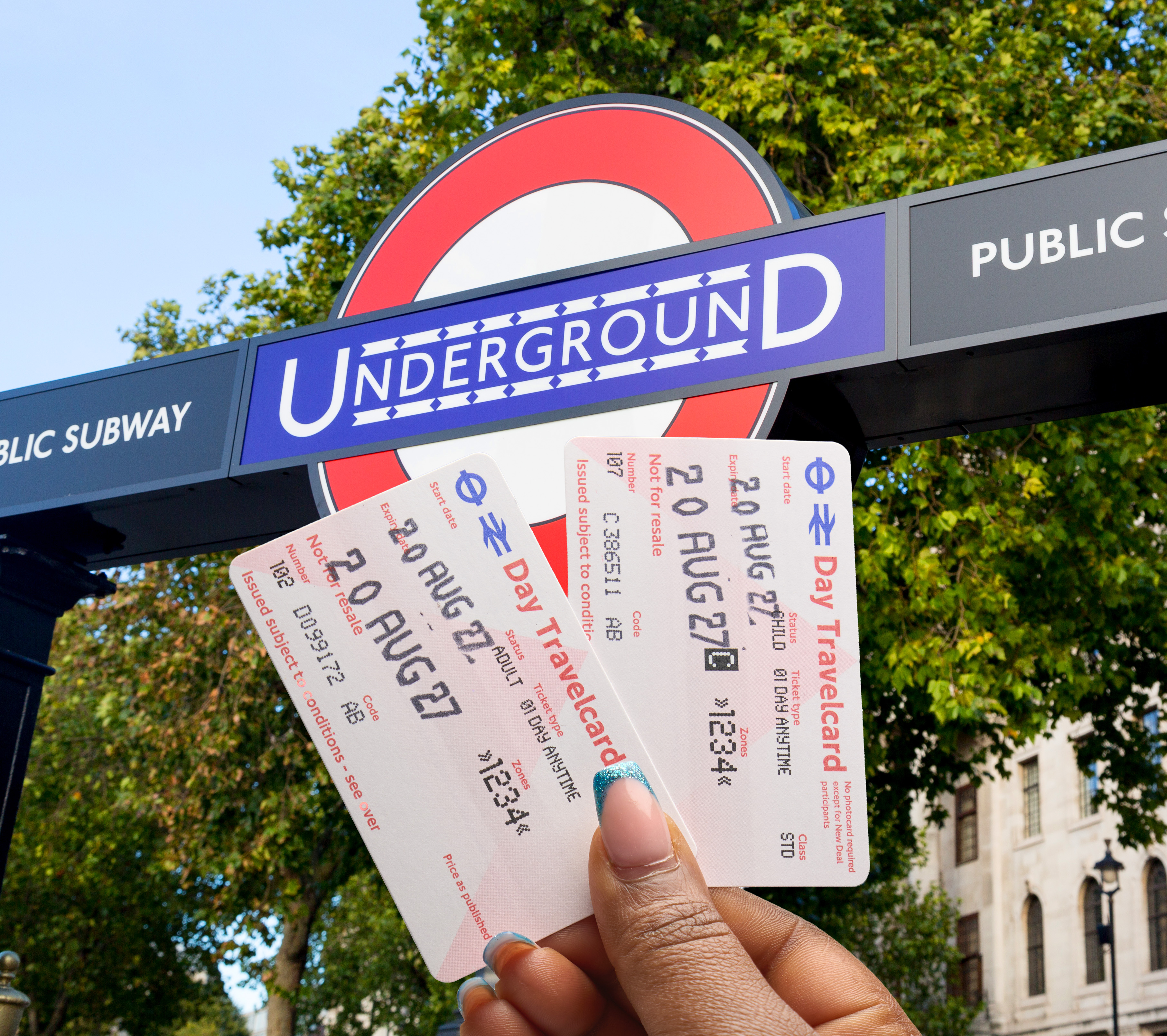 Zwei Tageskarten aufgefächert in Hand mit Underground Logo im Hintergrund in London