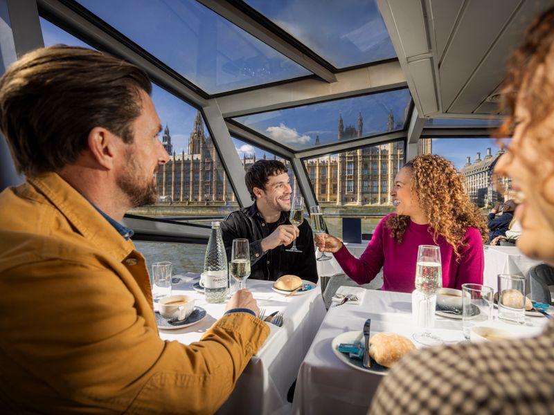 Gäste stoßen bei einer Lunch Cruise auf der Themse mit Blick auf die Houses of Parliament und Big Ben an