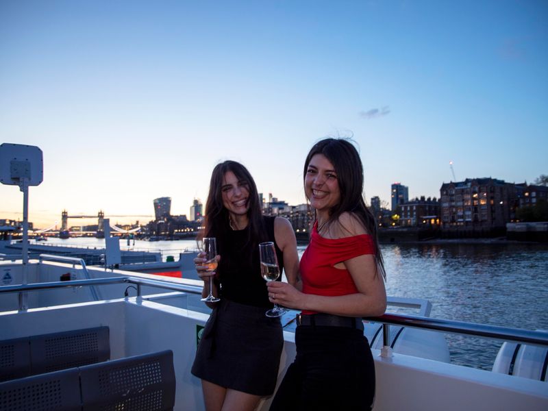 Zwei Gäste mit Sekt an Deck eines Schiffes mit der Tower Bridge im Hintergrund bei Sonnenuntergang