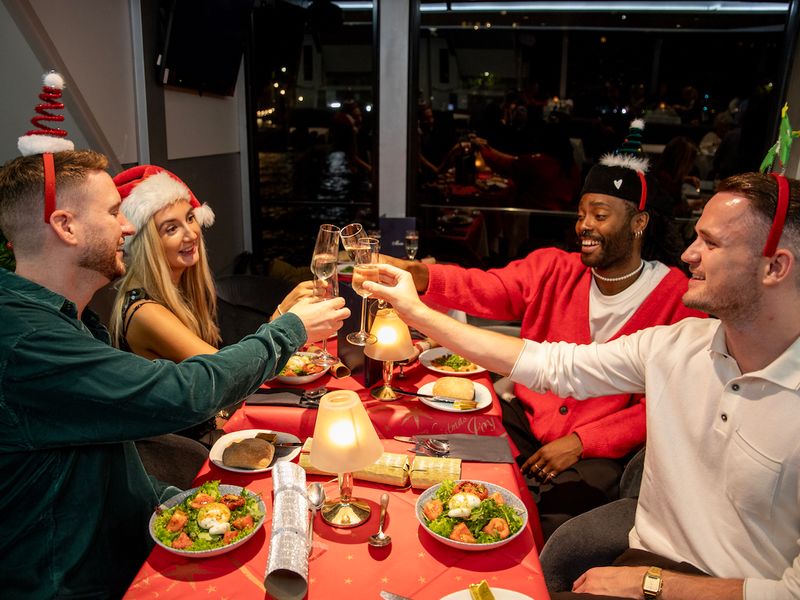 Freunde stoßen beim Weihnachtsessen während einer Dinner Cruise in London mit Sekt an
