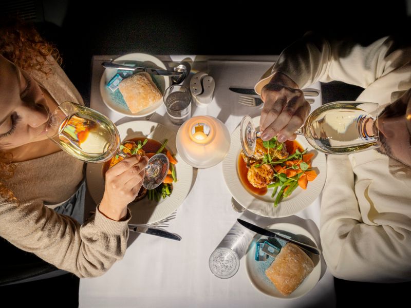 Zwei Gäste genießen Hauptgerichte und Weißwein während einer abendlichen Dinner Cruise in London