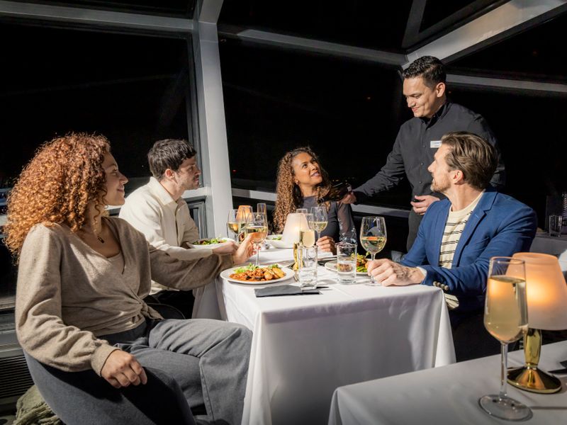 Gäste genießen ein serviertes Abendessen mit Wein bei einer Dinner Cruise auf der Themse in London
