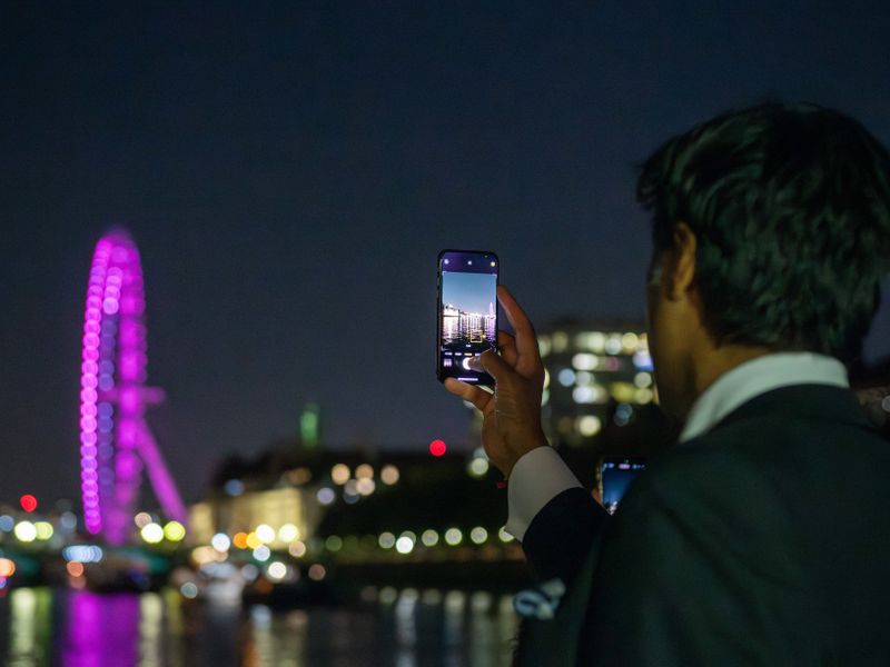 Gast fotografiert das beleuchtete London Eye während einer abendlichen Bootsfahrt auf der Themse