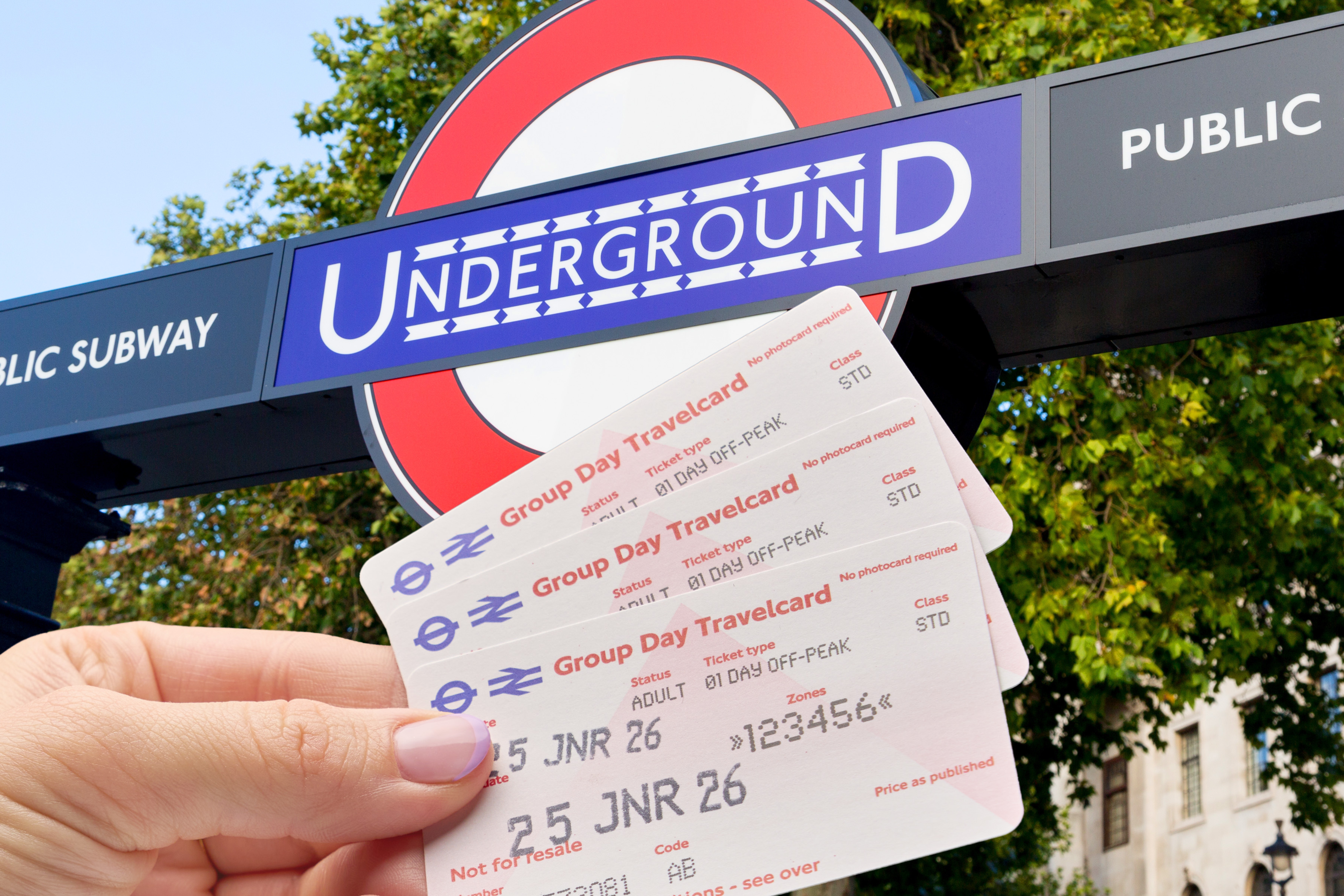 Drei Gruppenkarten aufgefächert in Hand mit Underground Logo im Hintergrund in London