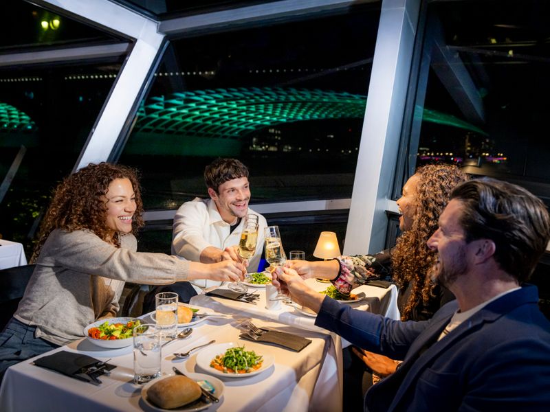 Vier Gäste stoßen bei einem Abendessen während einer abendlichen Themsefahrt in London mit Sekt an