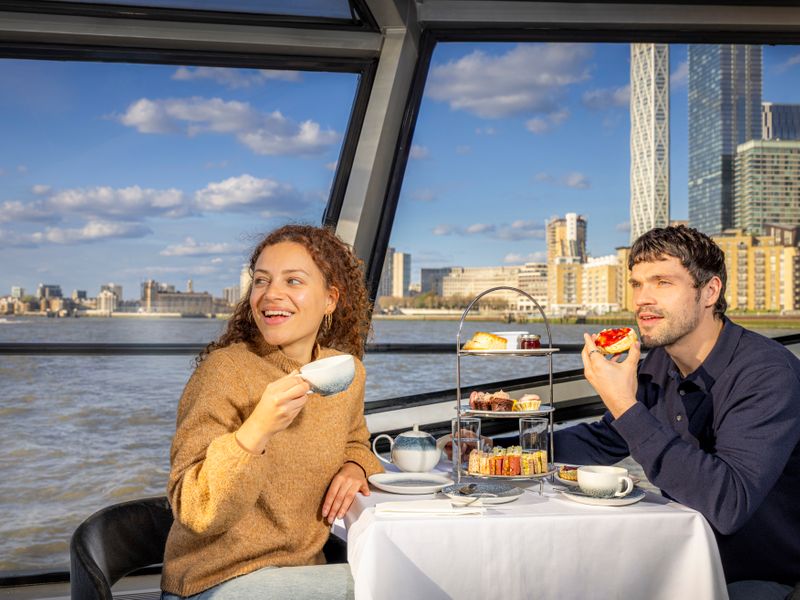 Zwei Gäste genießen Afternoon Tea am Fenster eines Schiffes mit Blick auf die Themse und die Londoner Skyline