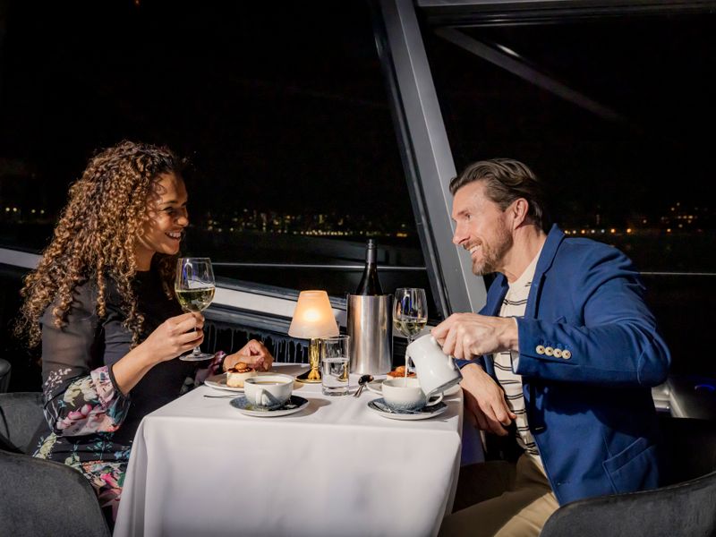 Paar genießt Wein und Dessert bei einem romantischen Dinner an Bord eines Schiffes auf der Themse