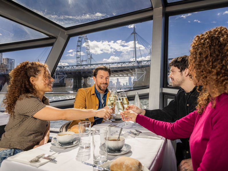 Vier Gäste stoßen bei einer Lunch Cruise auf der Themse mit Blick auf das London Eye an