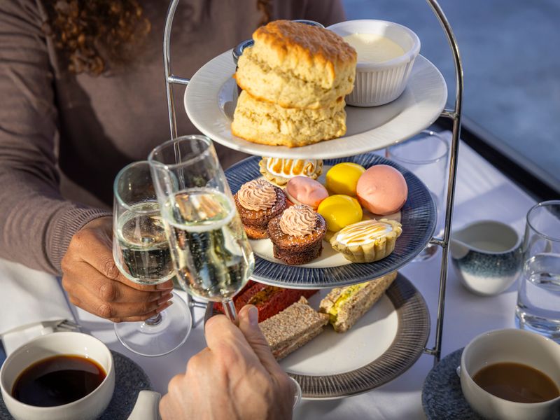 Etagere mit Scones, Kuchen und Sandwiches sowie zwei Gläsern Sekt bei einer Afternoon Tea Cruise in London